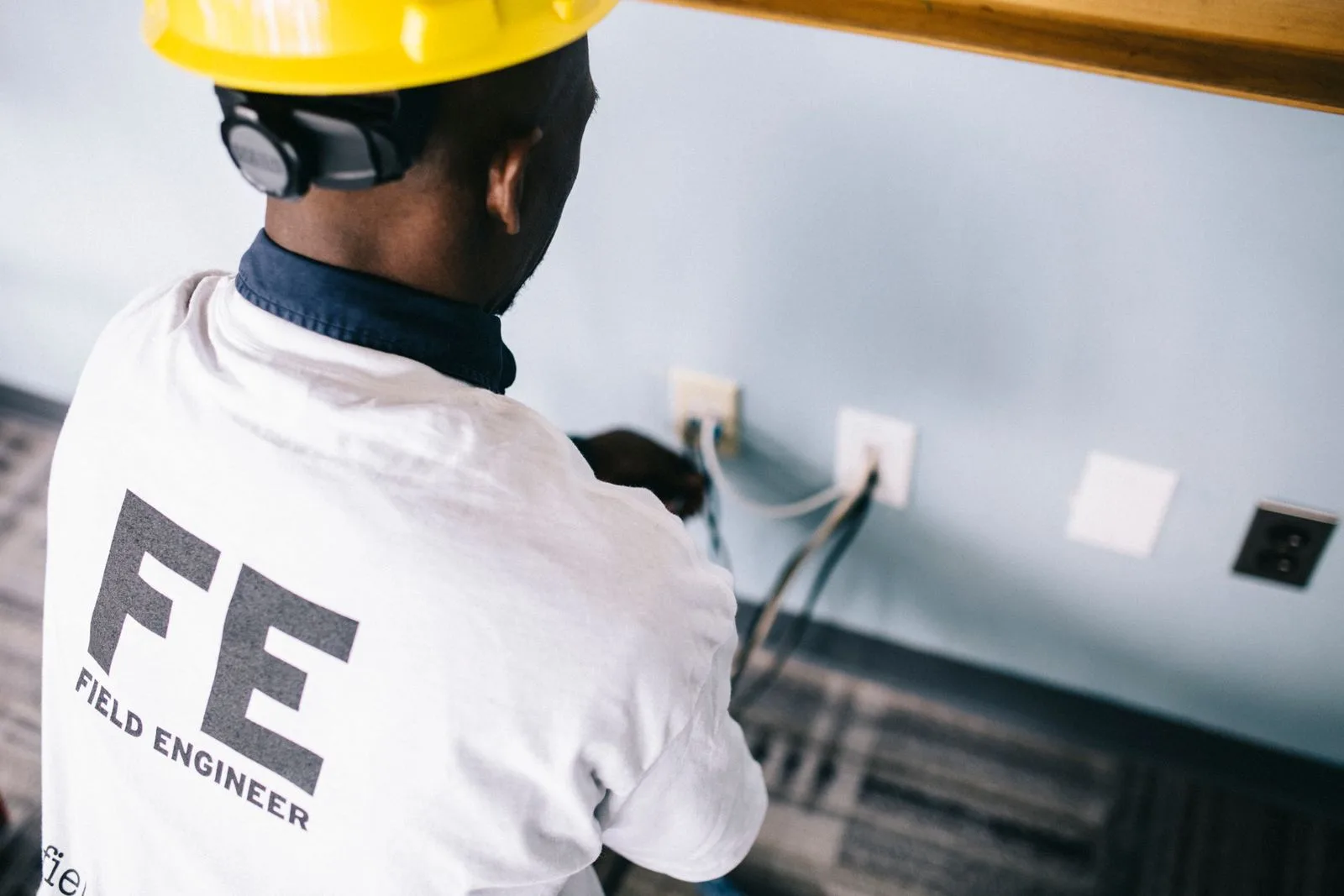 Elektriker mit Schutzhelm bei der Arbeit an einer Wandsteckdose