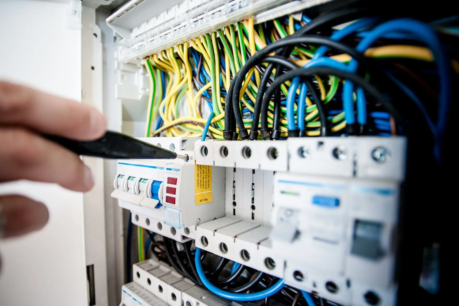 Hand eines Elektrikers justiert Sicherungsautomaten mit bunten Leitungen